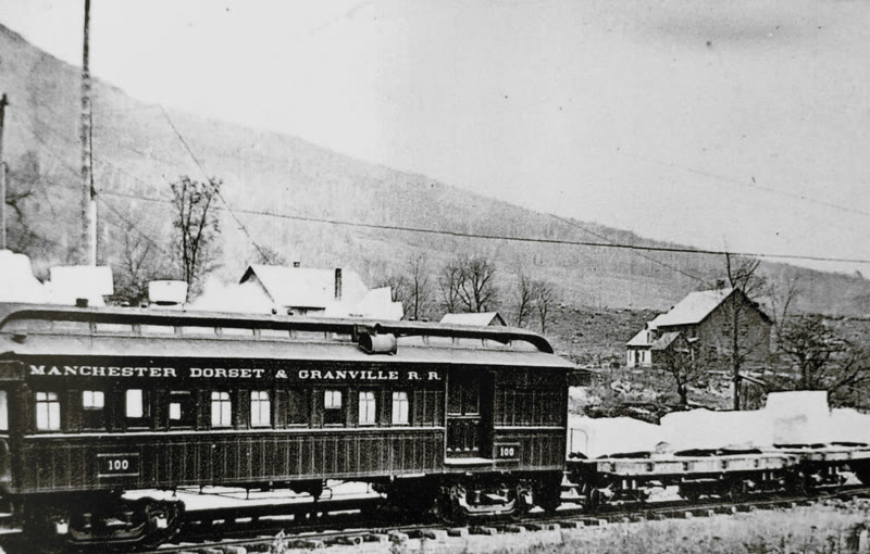 Historic photograph of Manchester, Dorset & Granville Railroad car No. 100, with flatcars of marble blocks behind it and a wooded hillside above